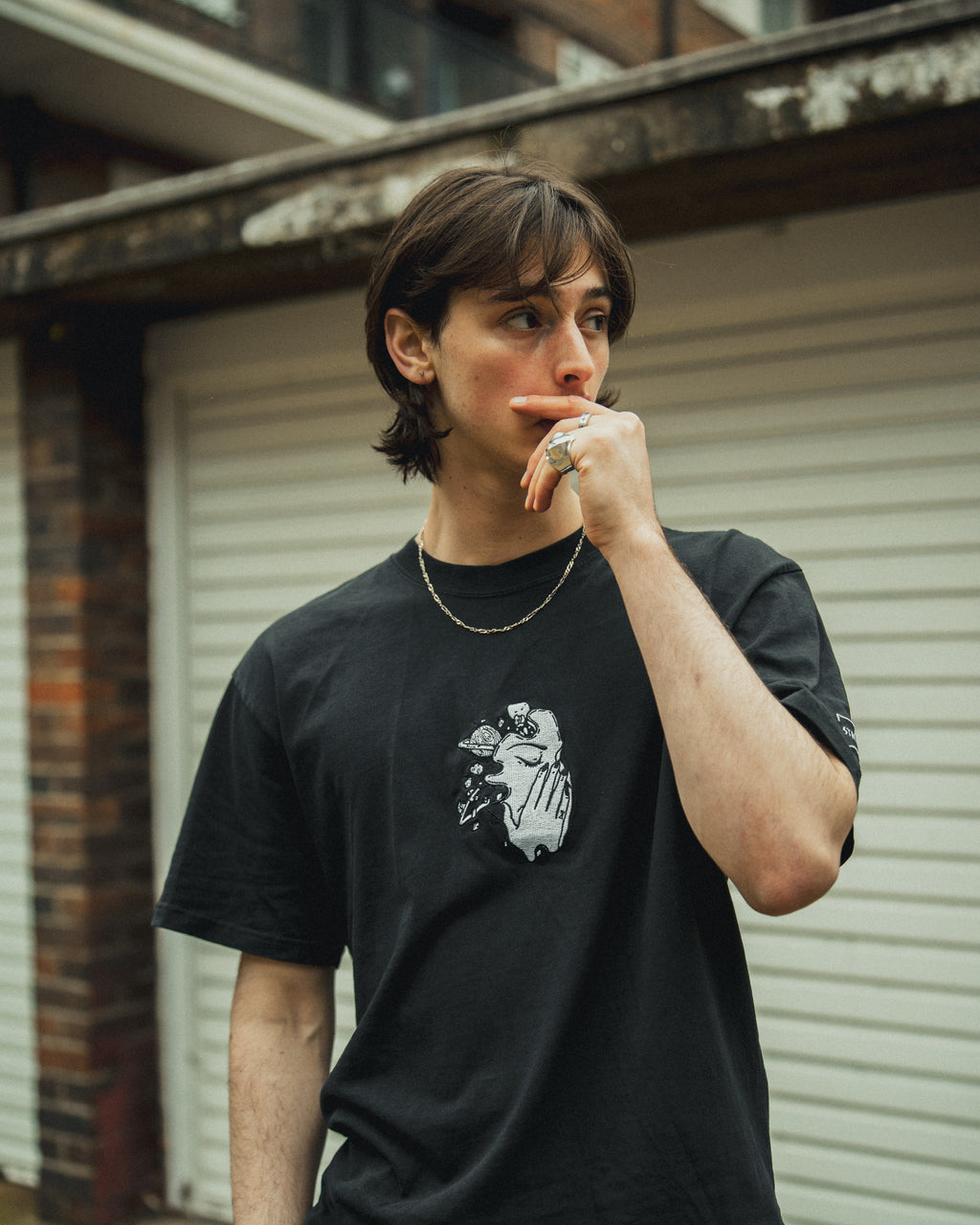 Oversized black STMNT Streetwear t-shirt with embroidered skull and floral design, worn by a young person with short, dark hair standing in a city setting.